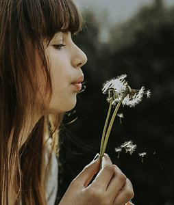 Reflections and Resources. Woman blowing dandelion seeds (cropped)